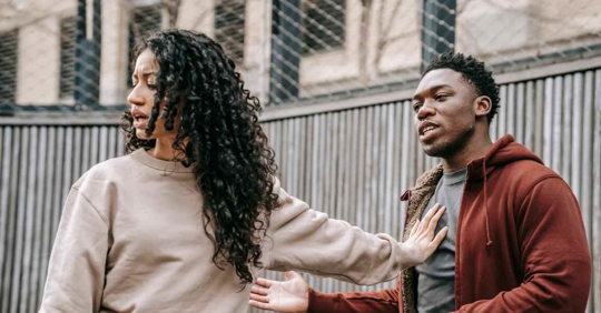A man and woman having an argument outside. The woman has her arm held out to the man's chest to keep him away from her