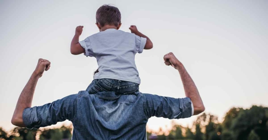 A father with his son on his shoulders. Both are flexing their biceps