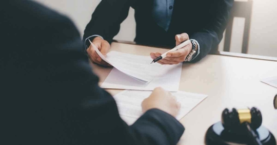 An attorney taking notes as another person sits across from them explaining their situation