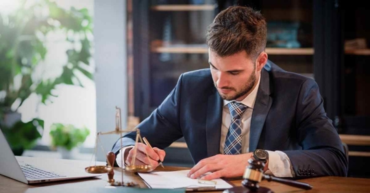 A male attorney sitting at a desk writing something on a piece of paper