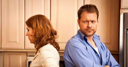 A man and woman standing back to back angrily against each other.
