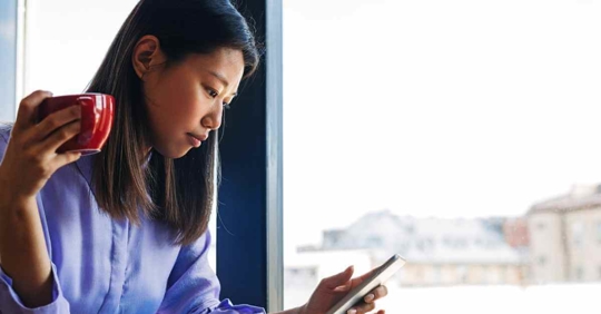 A woman reviewing something on her phone while holding a cup of coffee