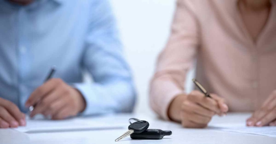 A man and woman filling out documents as a pair of car keys rests near them