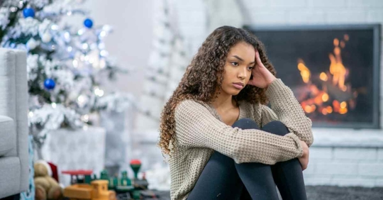 A sad woman sitting in front of a white Christmas tree