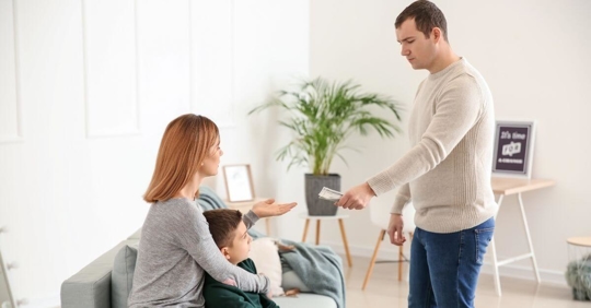 A man handing a woman money. The woman is guarding her son.