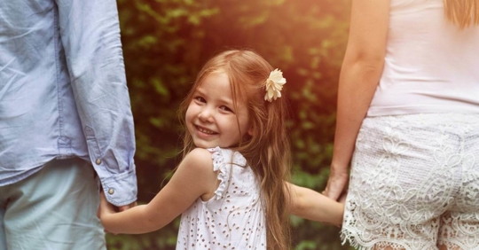 A young girl turning around and smiling as she walks with her parents.